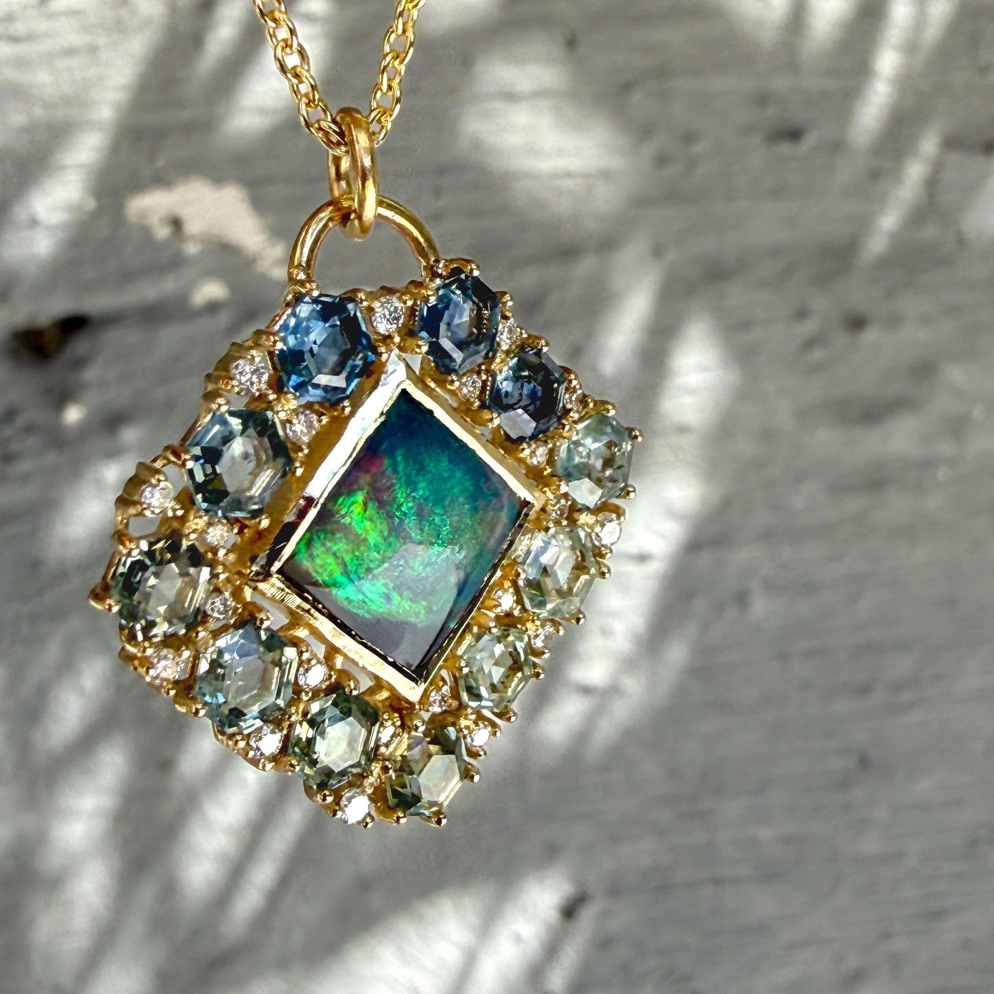 A three-quarter perspective captures an Australian Opal Pendant by NIXIN Jewelry. The side angle emphasizes the dimensional craftsmanship of the gold opal necklace and its protective bezel wall. Shifting light accentuates the rare opal jewelry piece alongside brilliant diamonds and custom geometric sapphires.