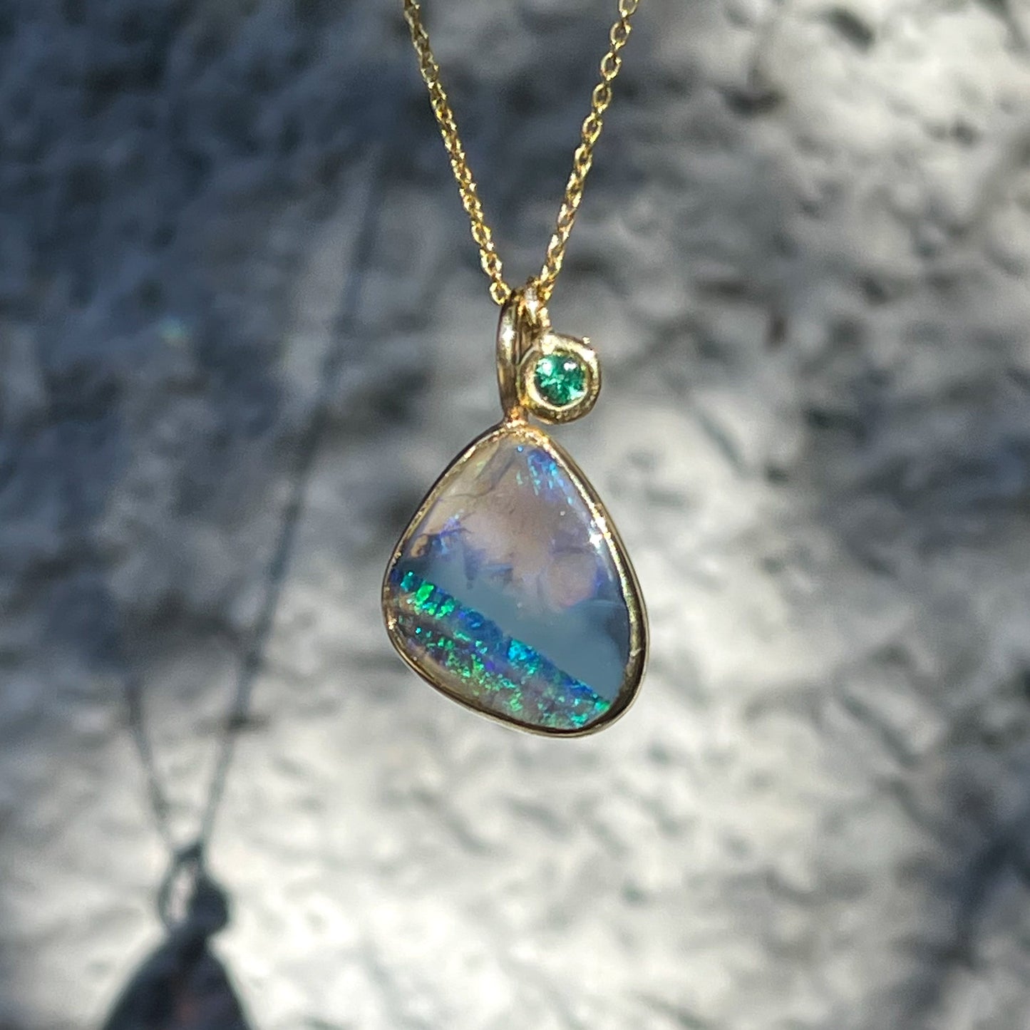 An Australian Opal Necklace by NIXIN Jewelry with a black opal stone and an emerald charm.