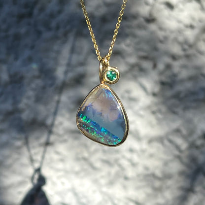 An Australian Opal Necklace by NIXIN Jewelry with a black opal stone and an emerald charm.