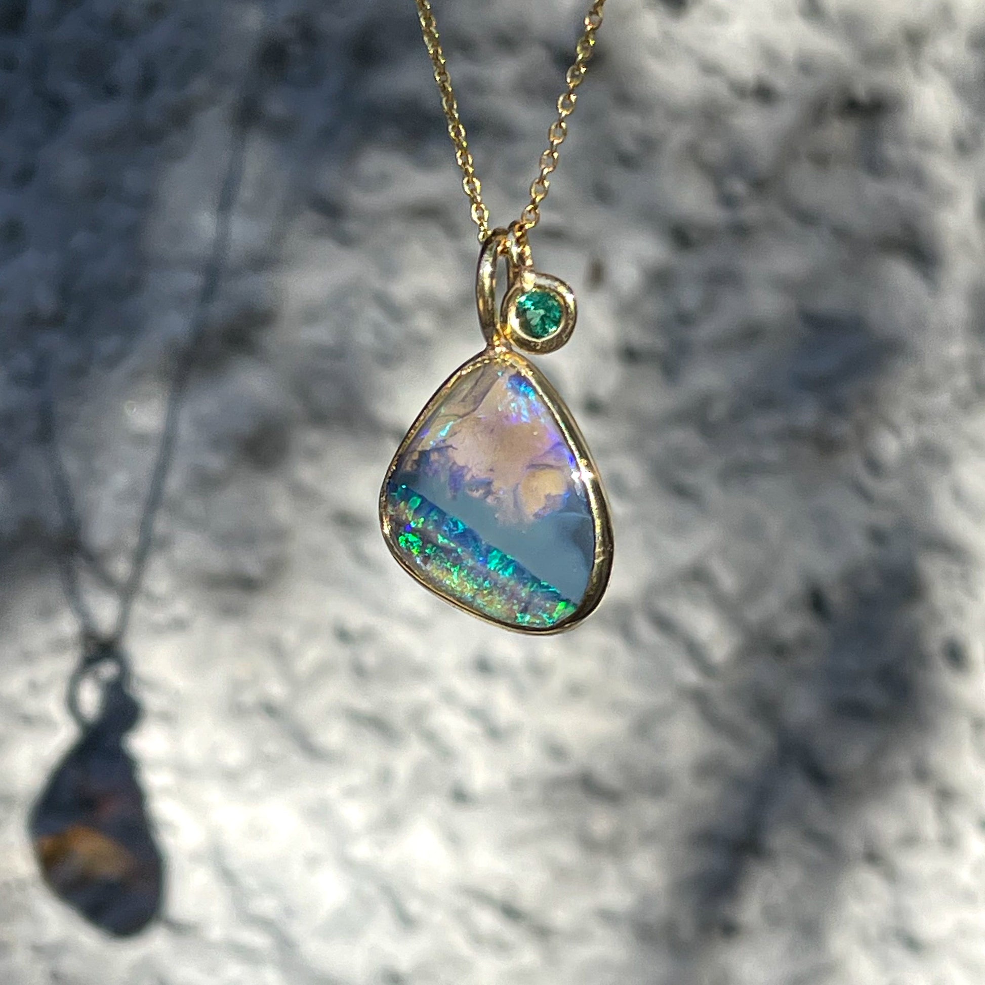 An Australian Opal Necklace by NIXIN Jewelry with a black crystal opal in a bezel setting and an emerald charm.