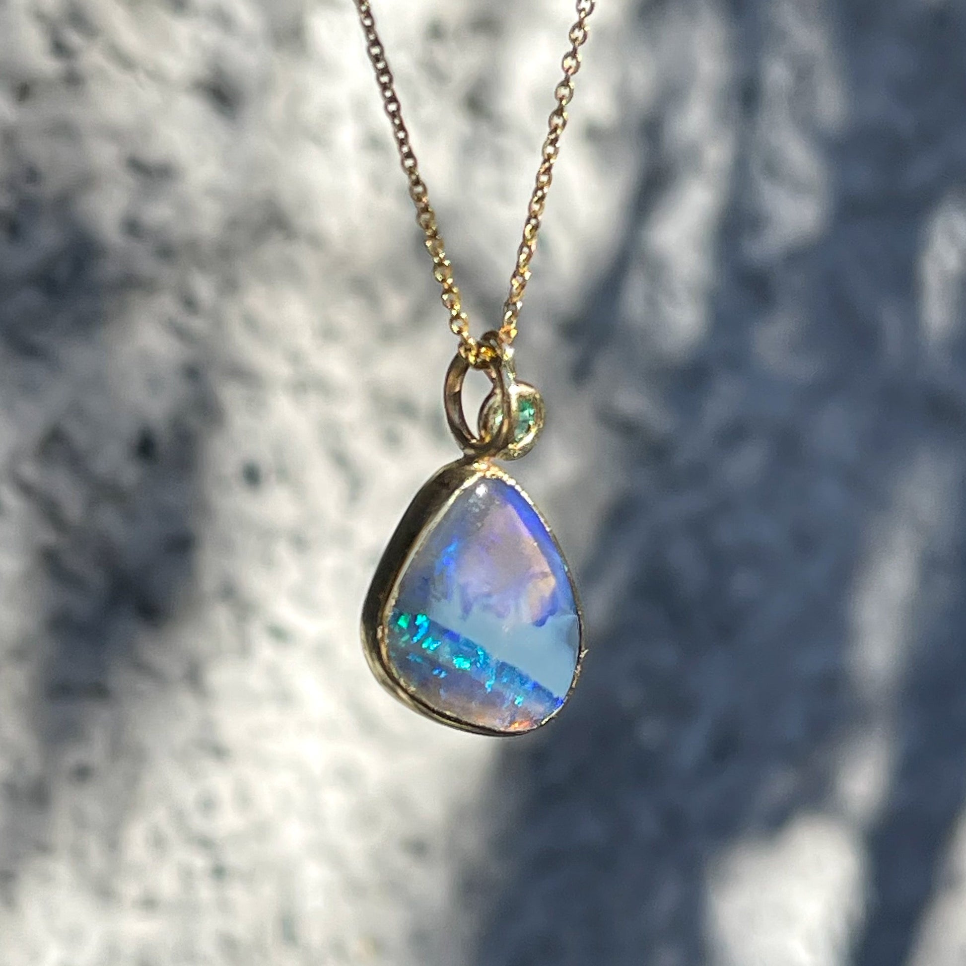 Angeld view of an Australian Opal Necklace by NIXIN Jewelry showing an opal stone and green emerald set in 14k gold.