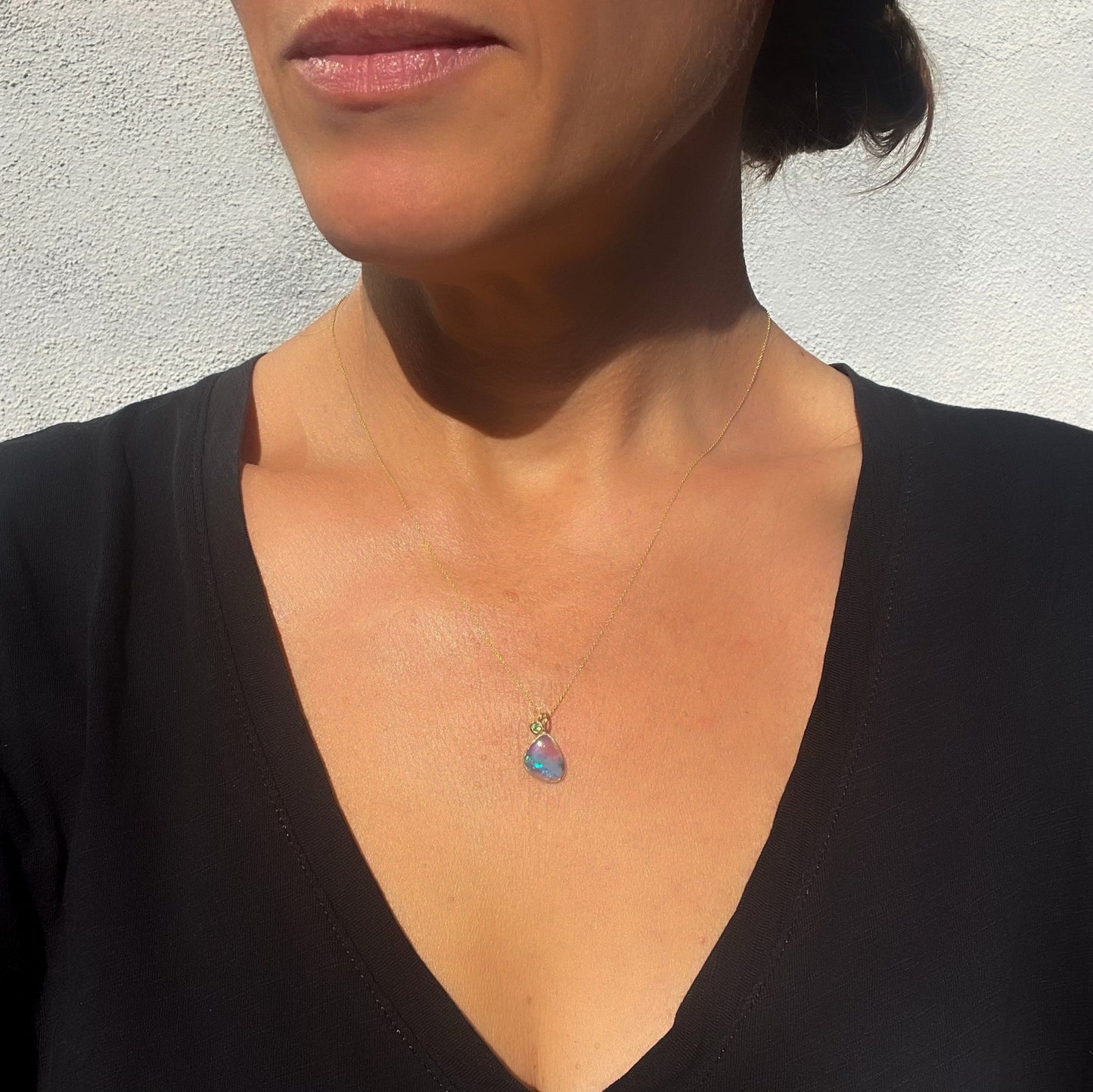 Model wearing an Australian Opal Necklace by NIXIN Jewelry made with a natural opal and a zambian emerald.
