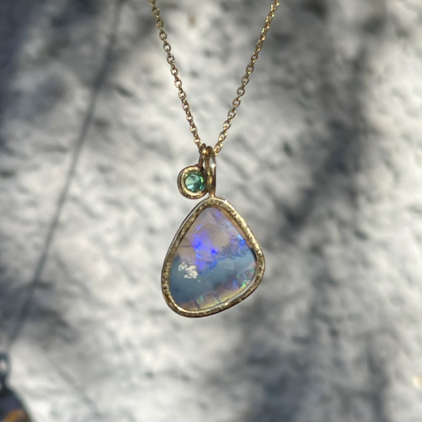 Back view of an Australian Opal Necklace by NIXIN Jewelry showing the open back of the bezel setting and the emerald stone charm.