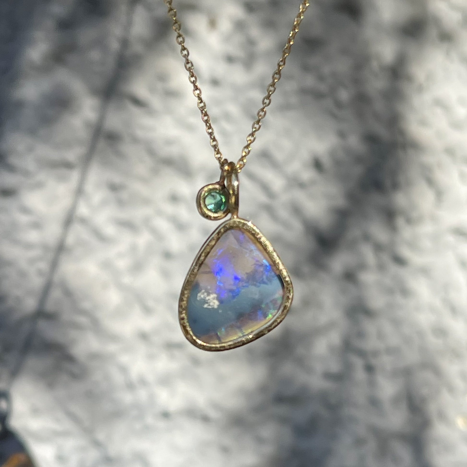 Back view of an Australian Opal Necklace by NIXIN Jewelry showing the open back of the bezel setting and the emerald stone charm.
