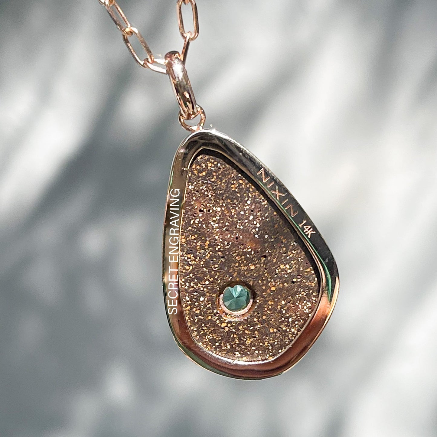 The back of an Australian Opal Necklace by NIXIN Jewelry hanging in front of a grey wall. The image shows where a secret engraving rests on the back of the bezel setting of the opal pendant necklace.