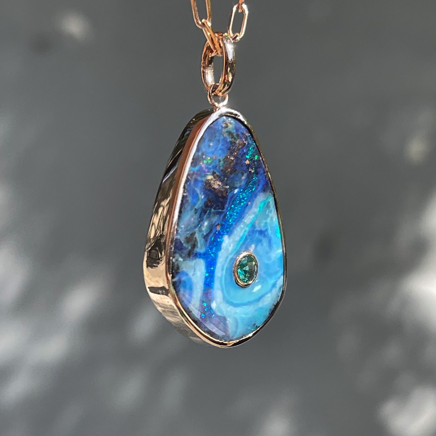 An Australian Opal Necklace by NIXIN Jewelry hanging in profile showing its bezel setting. The Boulder Opal has an emerald inlay.