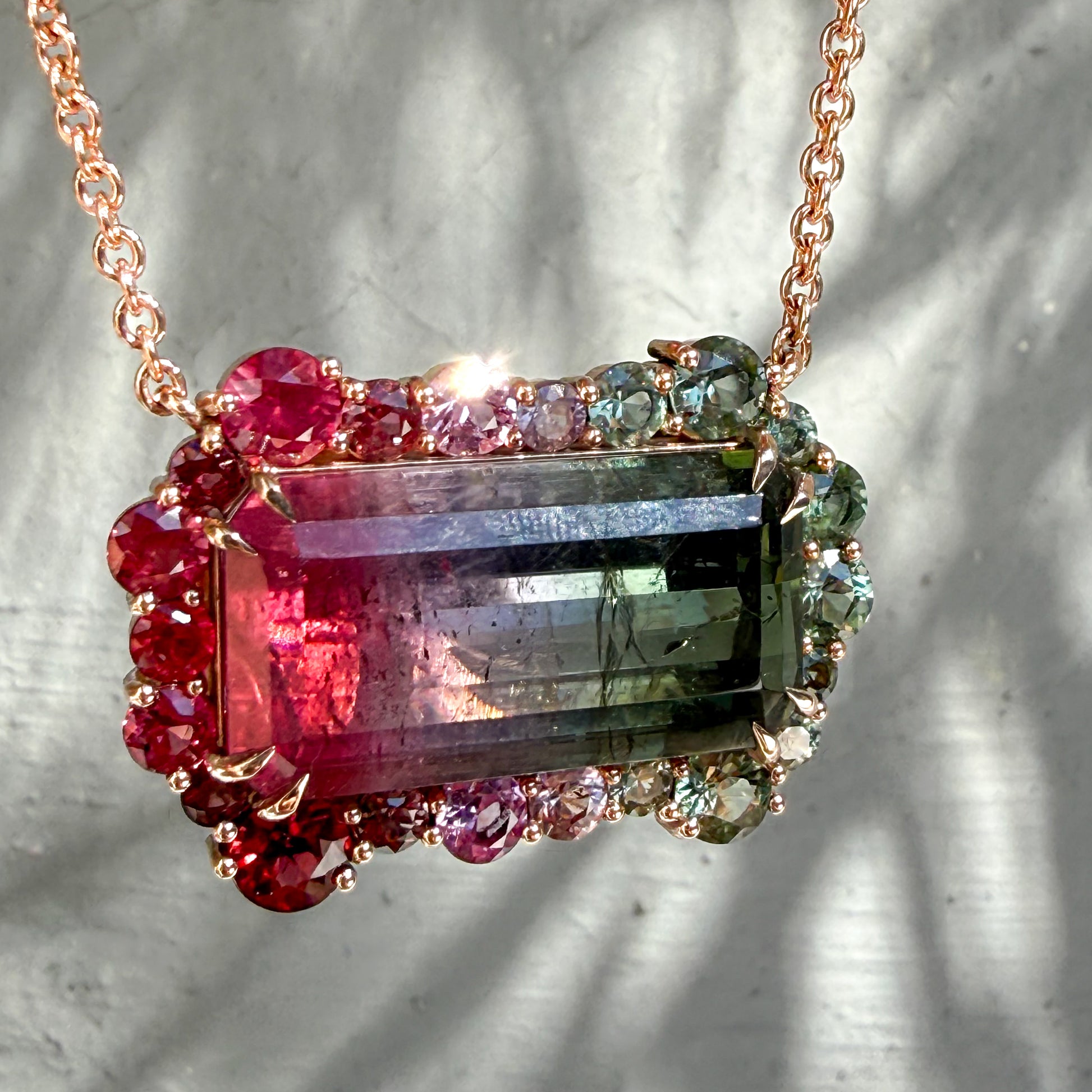 Angled detail of the Empress Imbued Tourmaline pendant by NIXIN Jewelry capturing light across the ruby and sapphire halo in soft daylight.