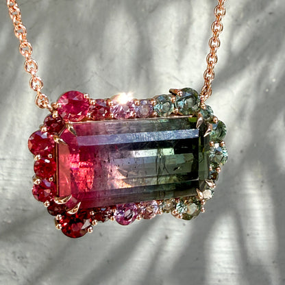 Angled detail of the Empress Imbued Tourmaline pendant by NIXIN Jewelry capturing light across the ruby and sapphire halo in soft daylight.