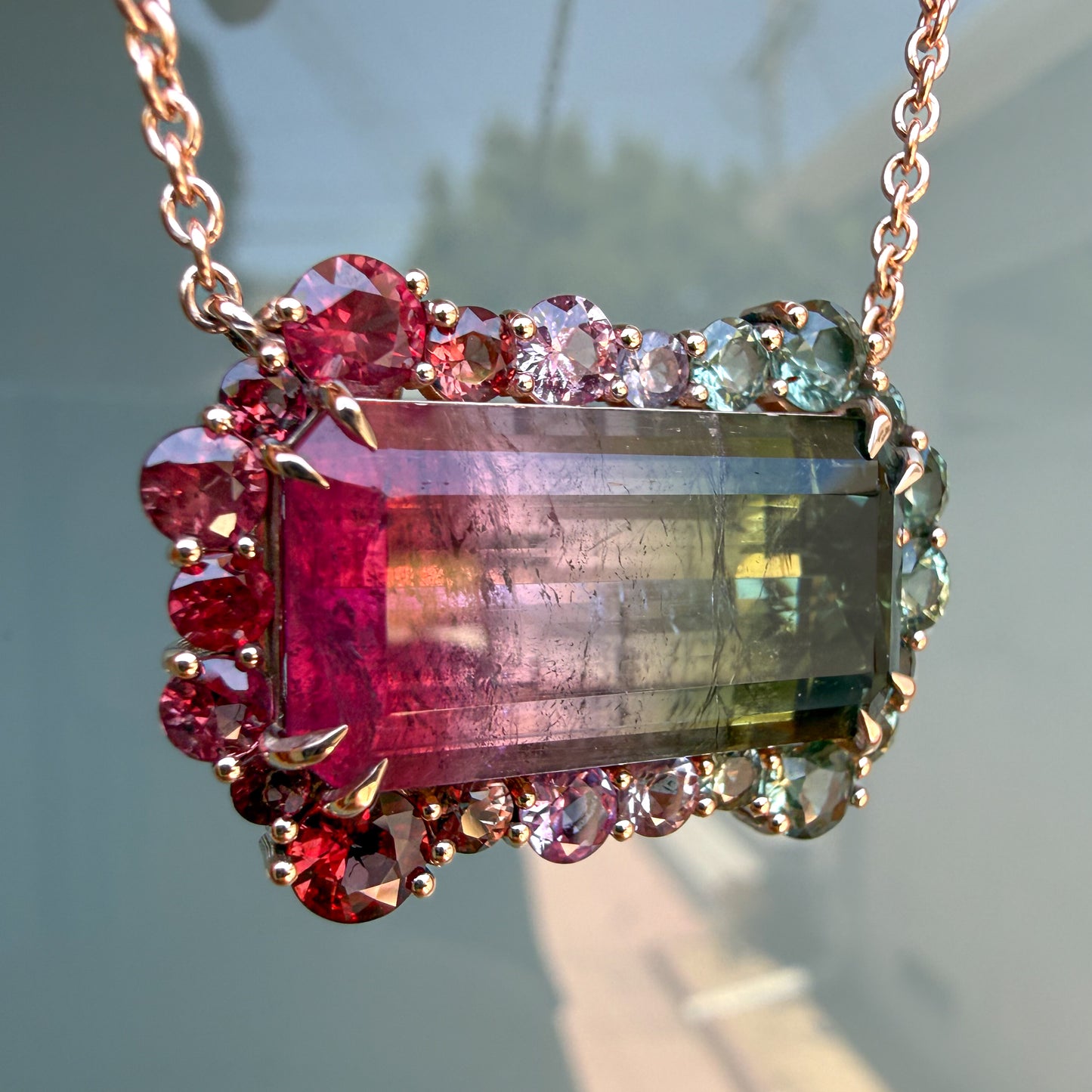 Tilted detail shot of the tourmaline pendant by NIXIN Jewelry highlighting the scalloped halo of rubies and pink and green sapphires.