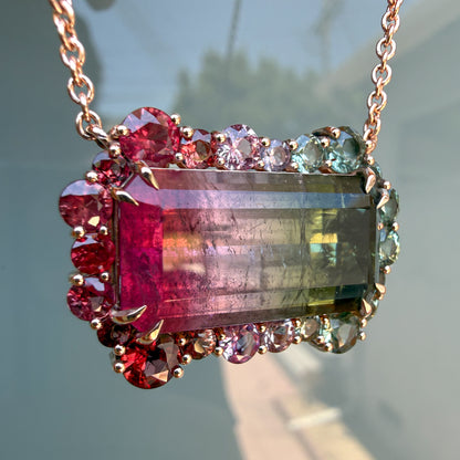 Tilted detail shot of the tourmaline pendant by NIXIN Jewelry highlighting the scalloped halo of rubies and pink and green sapphires.
