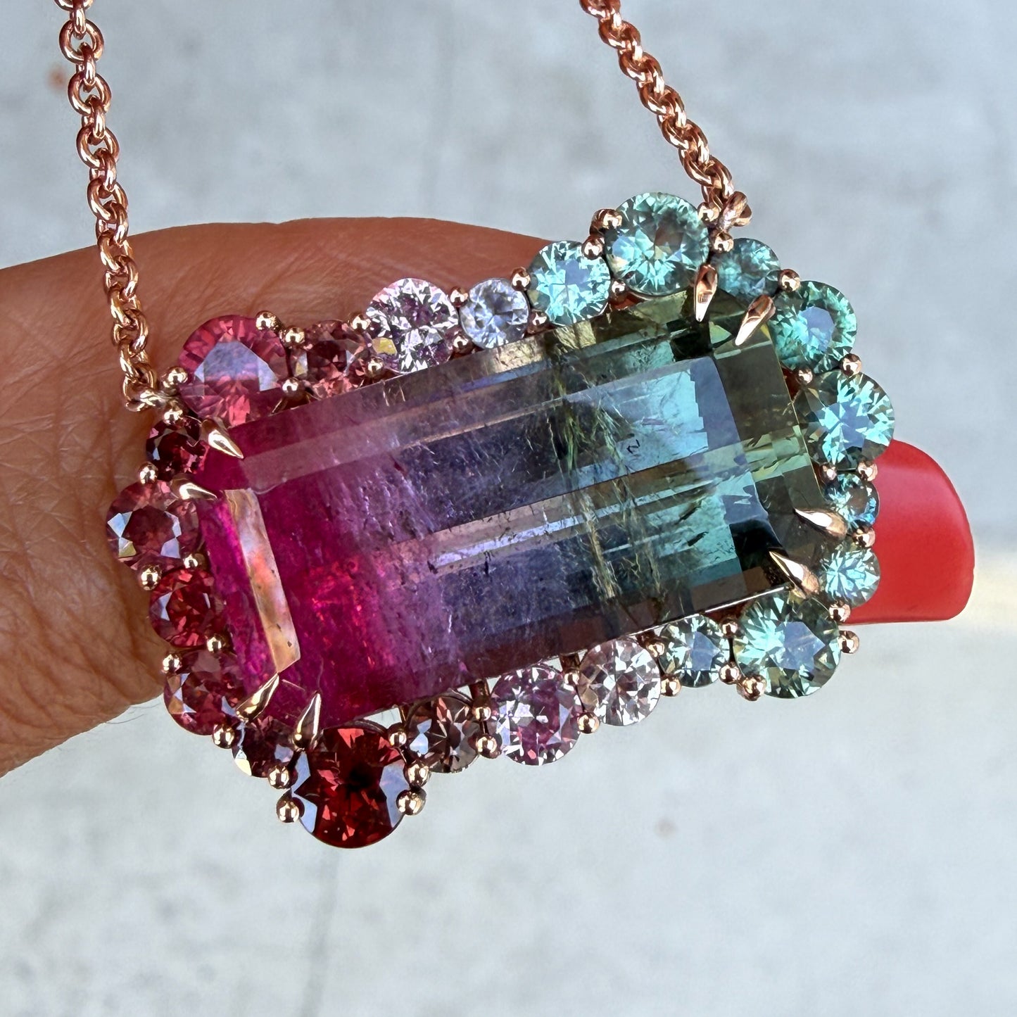 Empress Imbued Tourmaline Necklace pendant by NIXIN Jewelry held in shade, in hand at a profile angle, showing the transition from pink to green within the natural stone.