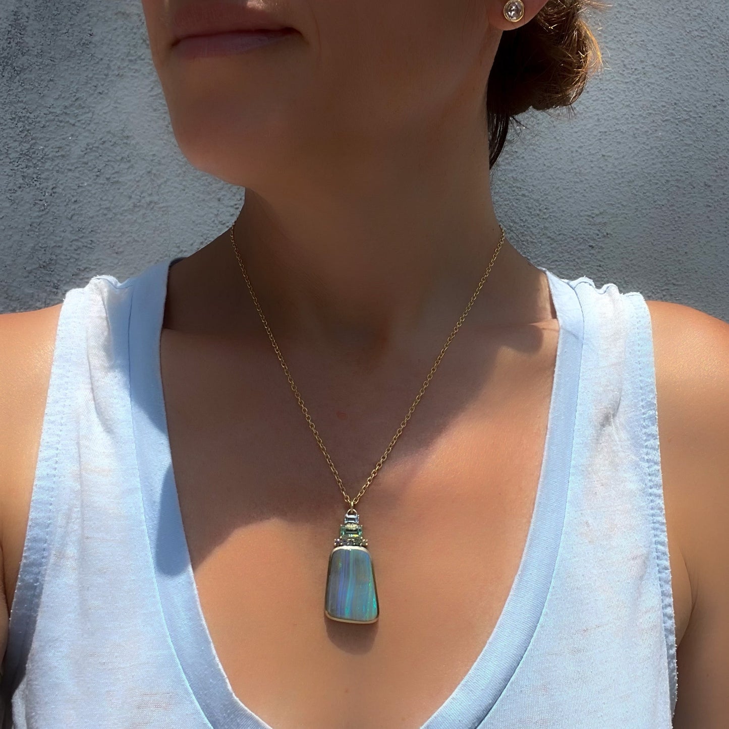 A model wearing an Australian Opal Necklace by NIXIN Jewelry. Gold opal necklace made with emerald, opal and sapphires.