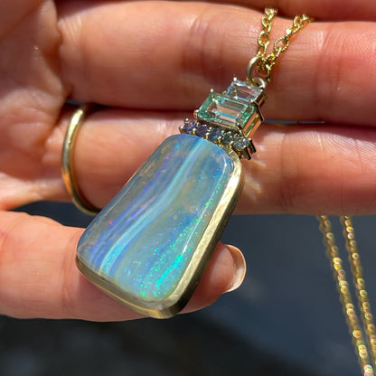An Australian Opal Necklace by NIXIN Jewelry shown at an angle, resting on a hand. The gold opal necklace combines opal with sapphire and emerald.