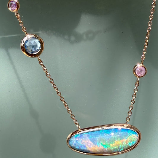 An Australian Opal Necklace by NIXIN Jewelry highlights the asymmetrical chain detailing with a blue rose cut sapphire and small pink sapphire accents. The combination of opal and sapphire creates an elegant opal necklace with a contemporary, artistic design.