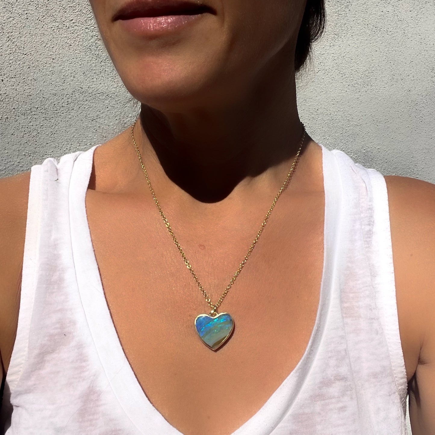 Model wearing an Australian Opal Necklace by NIXIN Jewelry with a blue opal heart set in 14k gold.