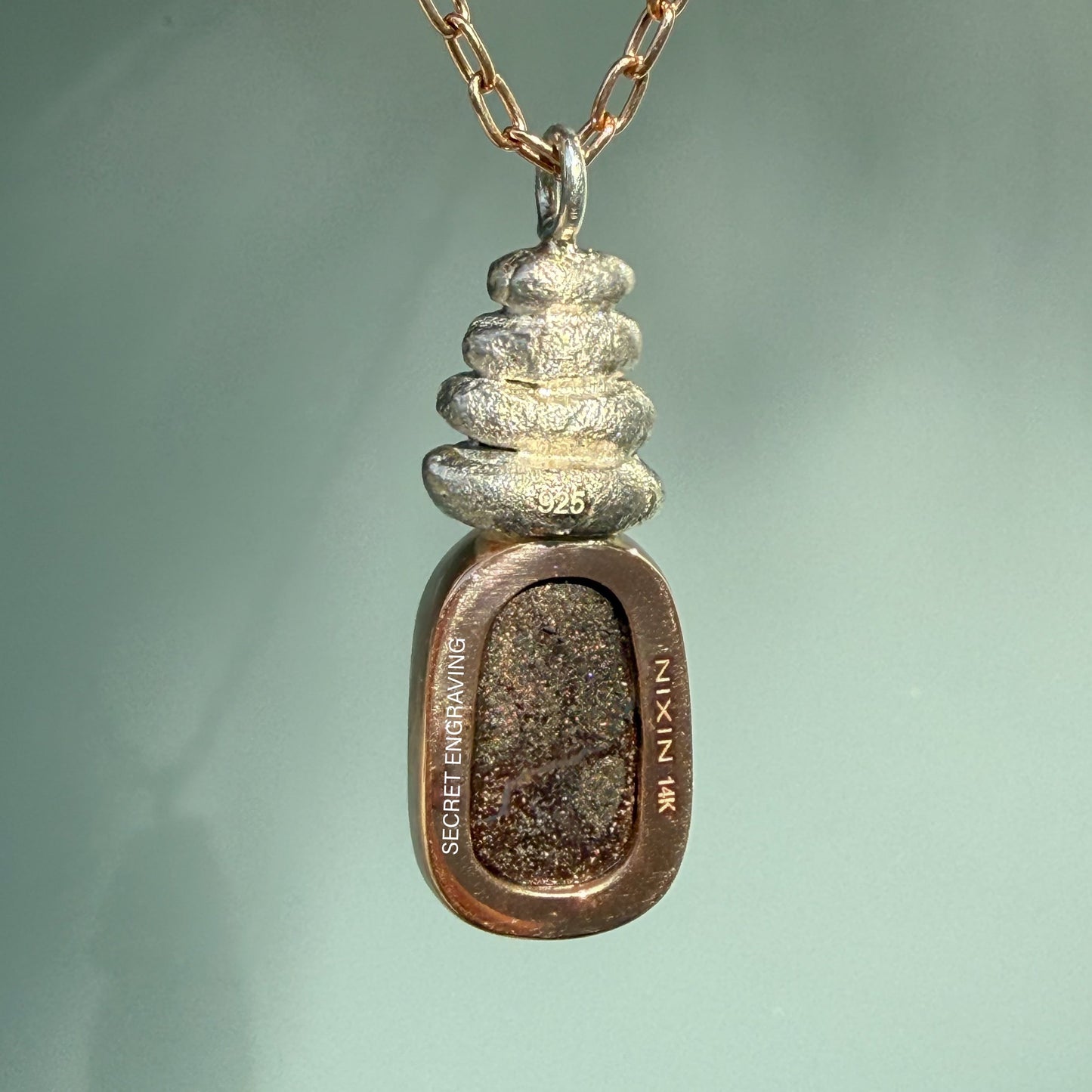 The reverse side of an Australian Opal Necklace by NIXIN Jewelry displays the "NIXIN 14K" and "925" hallmarks alongside a secret engraving. This luxury pendant necklace features an open-back design to reveal the natural ironstone matrix of the boulder opal. It ensures the wearer of the authenticity and premium quality of this rare jewelry piece.