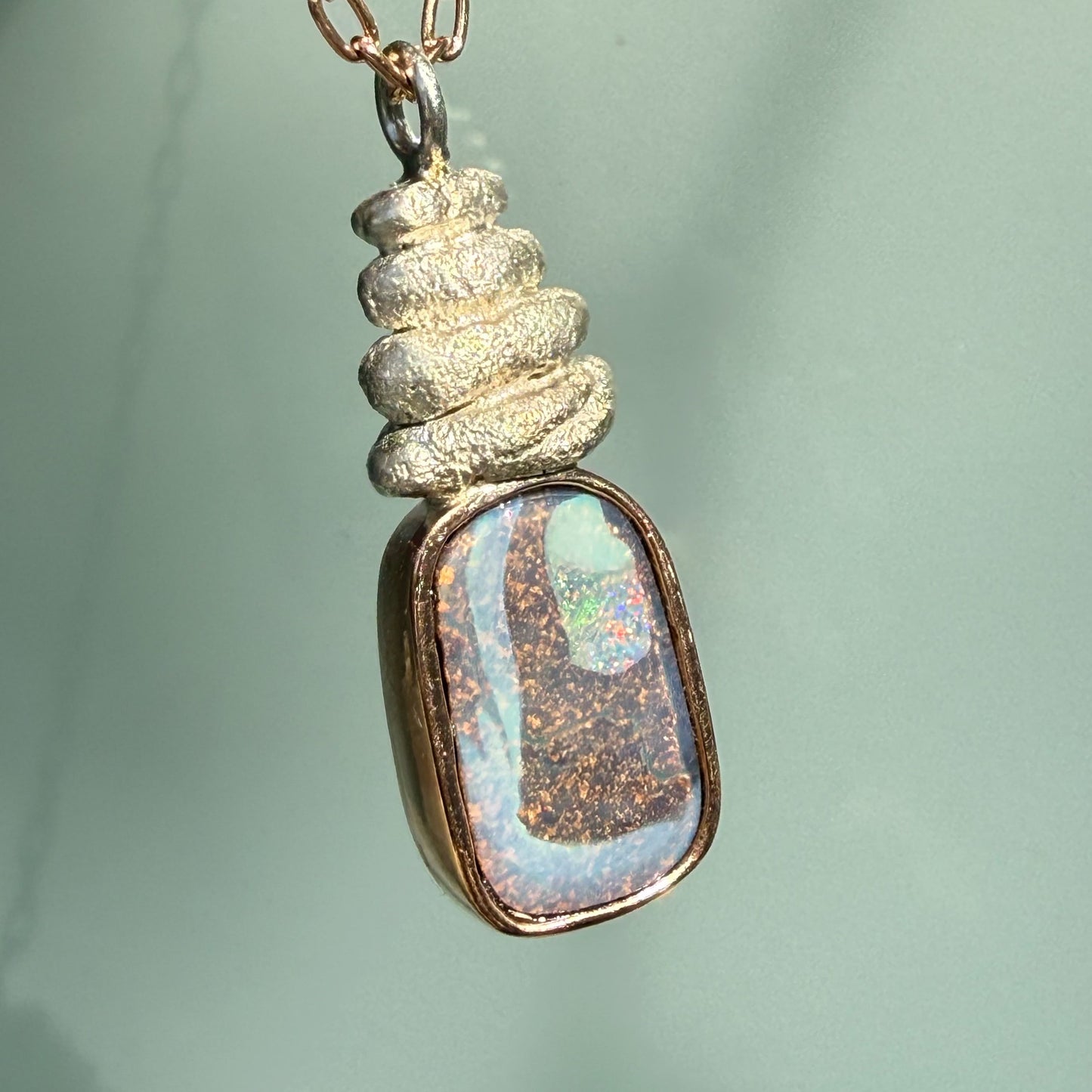 Hanging at an angle, this Australian Opal Necklace by NIXIN Jewelry beautifully demonstrates the harmony of mixed metal jewelry. The rose gold opal necklace features a polished finish that contrasts with the textured, sculptural silver elements of the pendant. This elegant opal necklace is a versatile addition to any luxury jewelry collection.