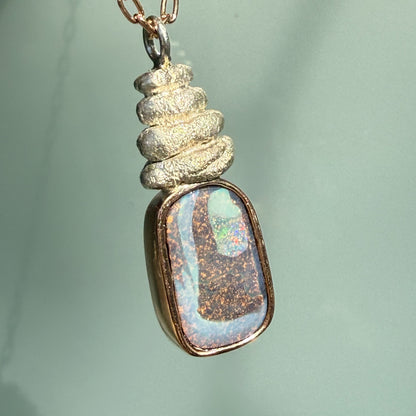 Hanging at an angle, this Australian Opal Necklace by NIXIN Jewelry beautifully demonstrates the harmony of mixed metal jewelry. The rose gold opal necklace features a polished finish that contrasts with the textured, sculptural silver elements of the pendant. This elegant opal necklace is a versatile addition to any luxury jewelry collection.