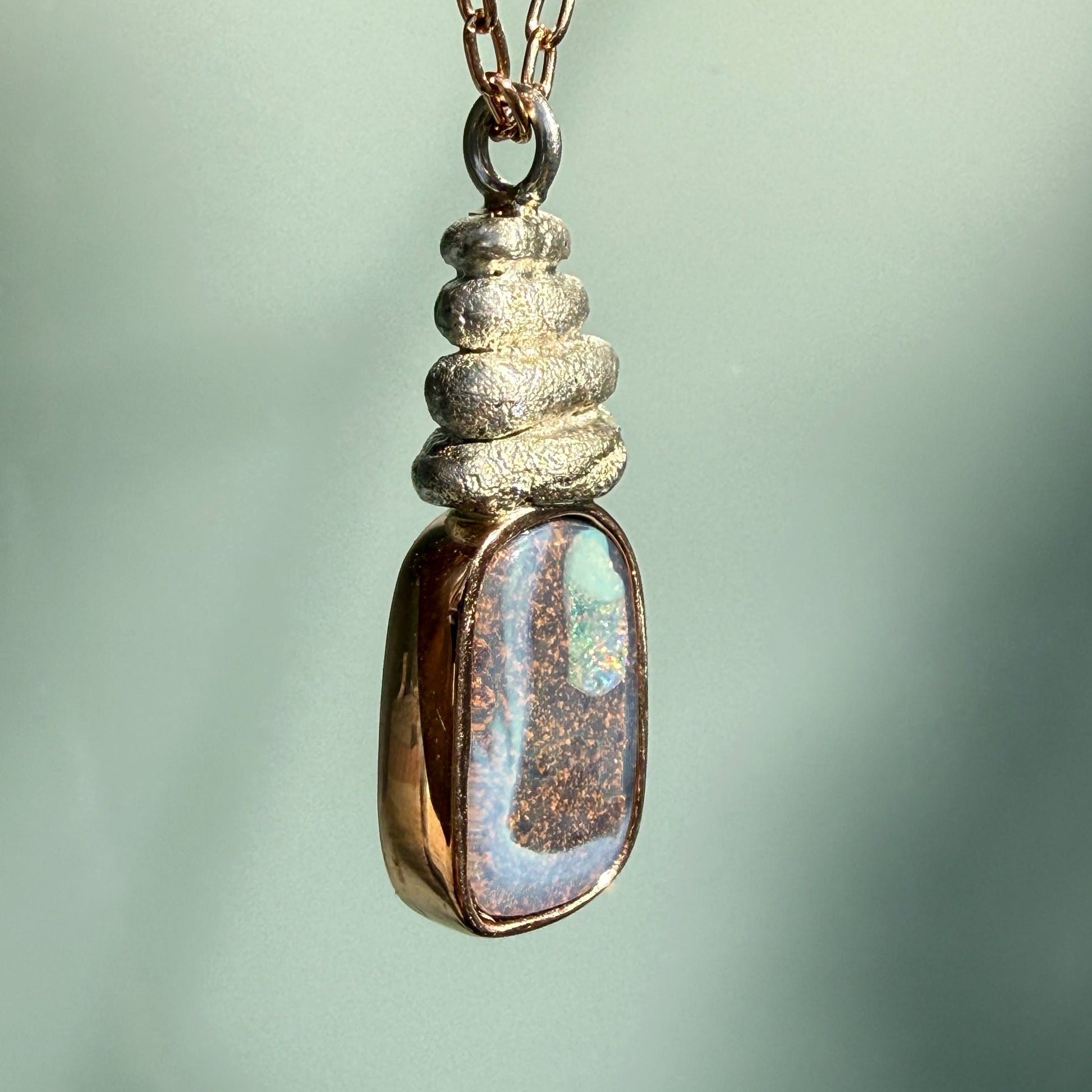 Seen from a side profile, this is an Australian Opal Necklace by NIXIN Jewelry showing the substantial depth of the 14k rose gold bezel and silver setting. The luxury necklace construction is robust yet refined, showcasing the solid boulder opal necklace craftsmanship. This unique fine jewelry piece is built to be a lasting heirloom jewelry staple.