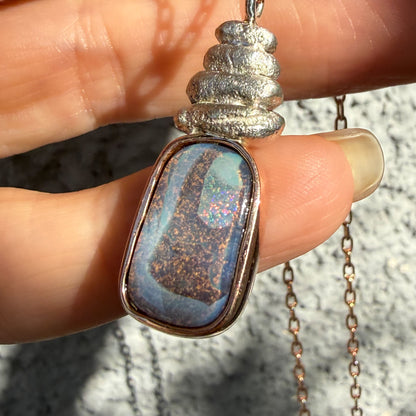 Showcasing play of color in natural light, this Australian Opal Necklace by NIXIN Jewelry is held to reveal its pink and green flashes. The unique opal necklace highlights a boulder opal picture stone secured in a protective bezel setting. This rare jewelry piece is perfect for those seeking a natural opal with a distinctive personality.