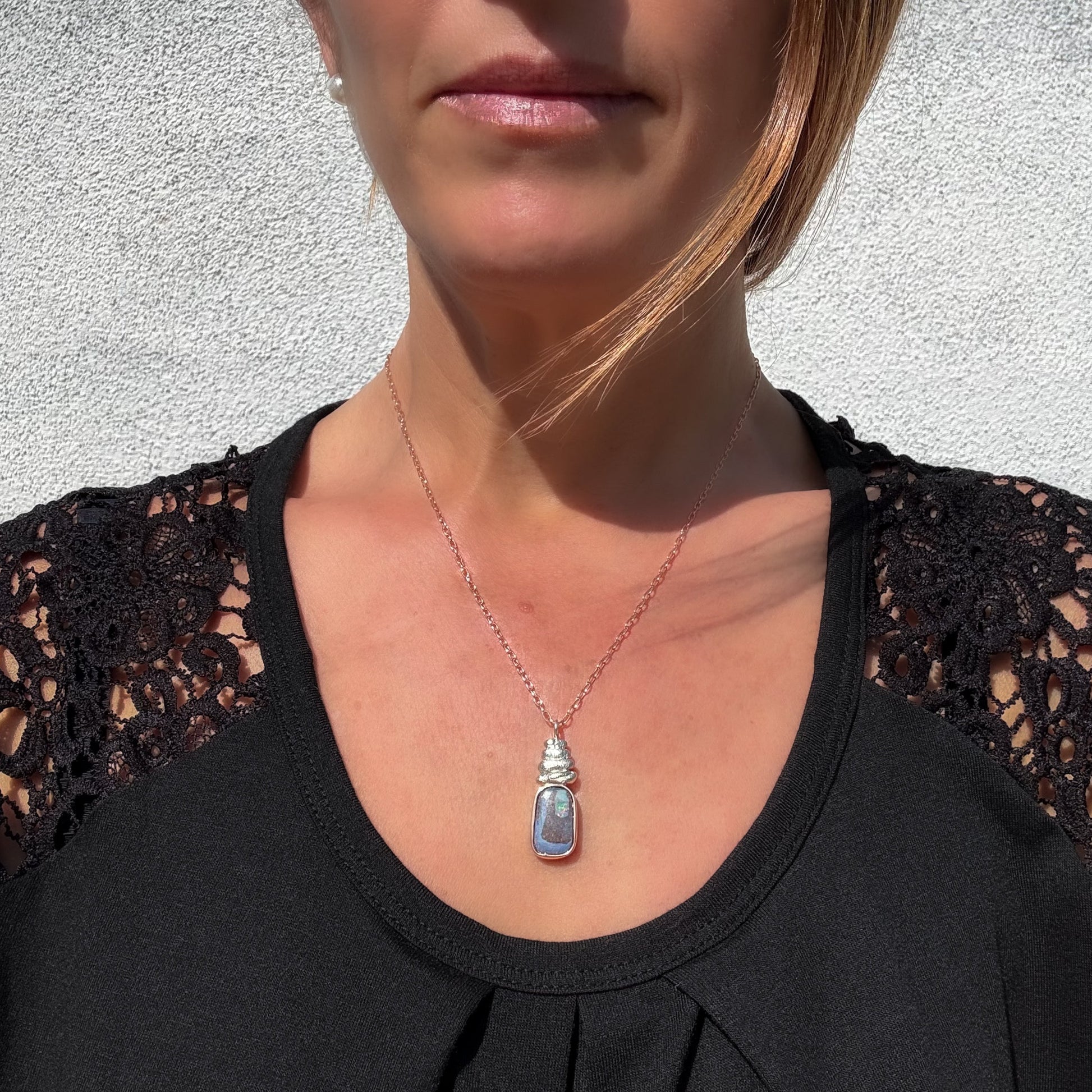 This is an Australian Opal Necklace by NIXIN Jewelry modeled to show its scale and placement on a woman’s neckline. The women's luxury necklace features a one-of-a-kind boulder opal set in a mixed metal design of 14k rose gold and silver. It is a sophisticated example of unique fine jewelry designed for the modern luxury consumer.
