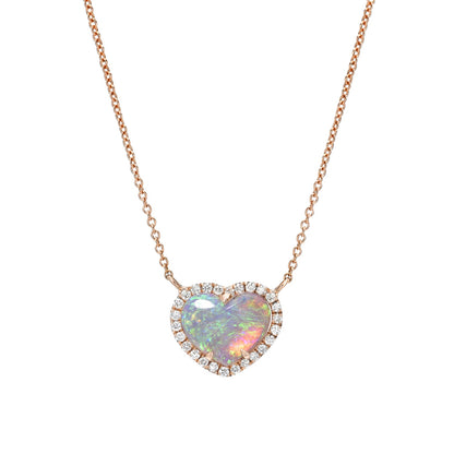 An Opal Heart Necklace by NIXIN Jewelry hanging in front of a white backdrop. The necklace is made with a Crystal Opal and diamonds in 14k rose gold.
