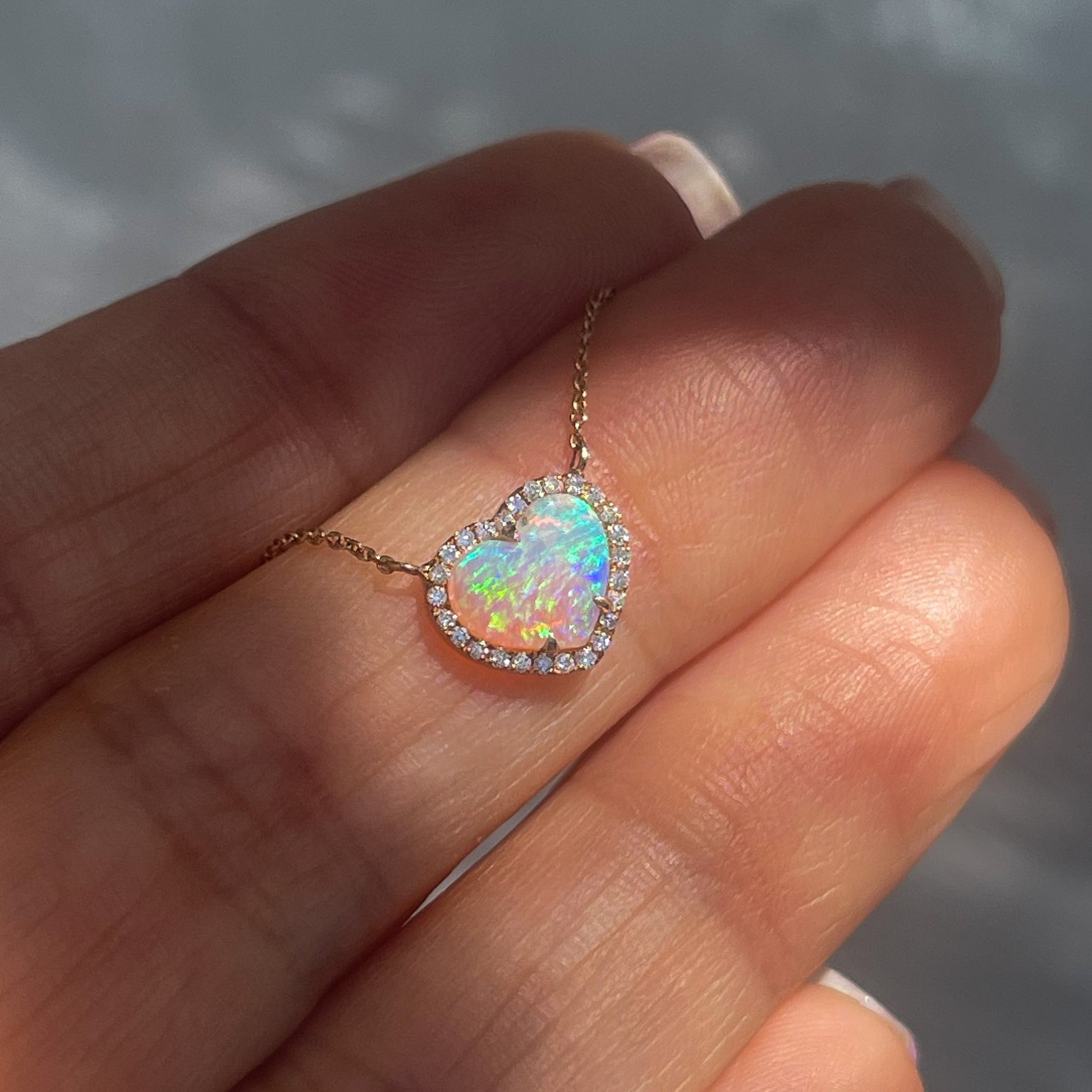 An Opal Heart Necklace by NIXIN Jewelry shown on top of a hand. The rose gold opal necklace is multicolored and has diamonds.