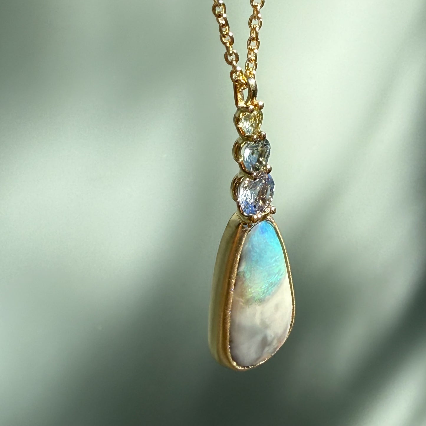 An angled shot of an Australian Opal Pendant by NIXIN Jewelry accented with genuine sapphires capping the stone, creating a stunning gradient effect. This specialized design highlights the unique jewelry nature of NIXIN's rare opal necklace offerings.