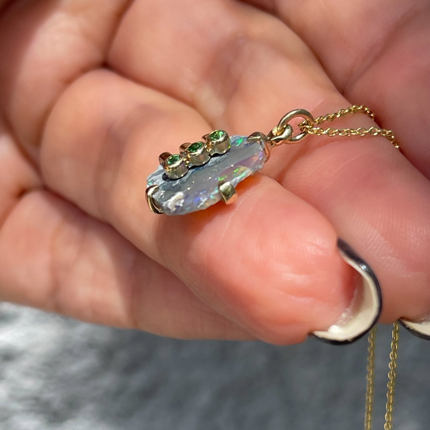 Side view of an Australian Opal Necklace by NIXIN Jewelry with a Black Opal and green gemstones. 