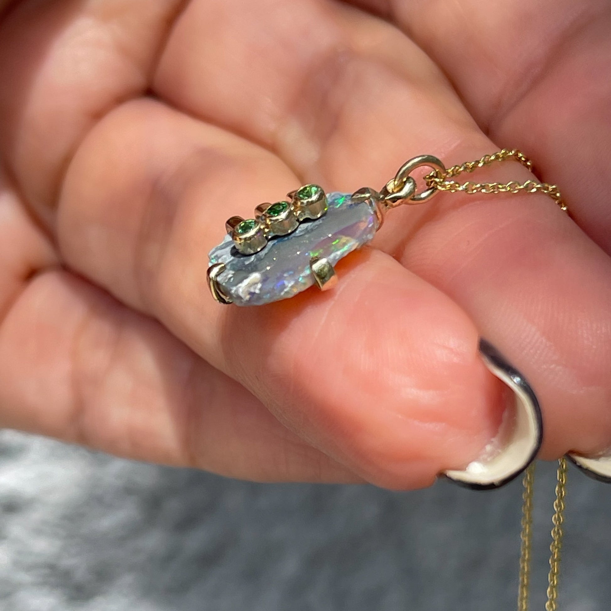 Side view of an Australian Opal Necklace by NIXIN Jewelry with a Black Opal and green gemstones. 