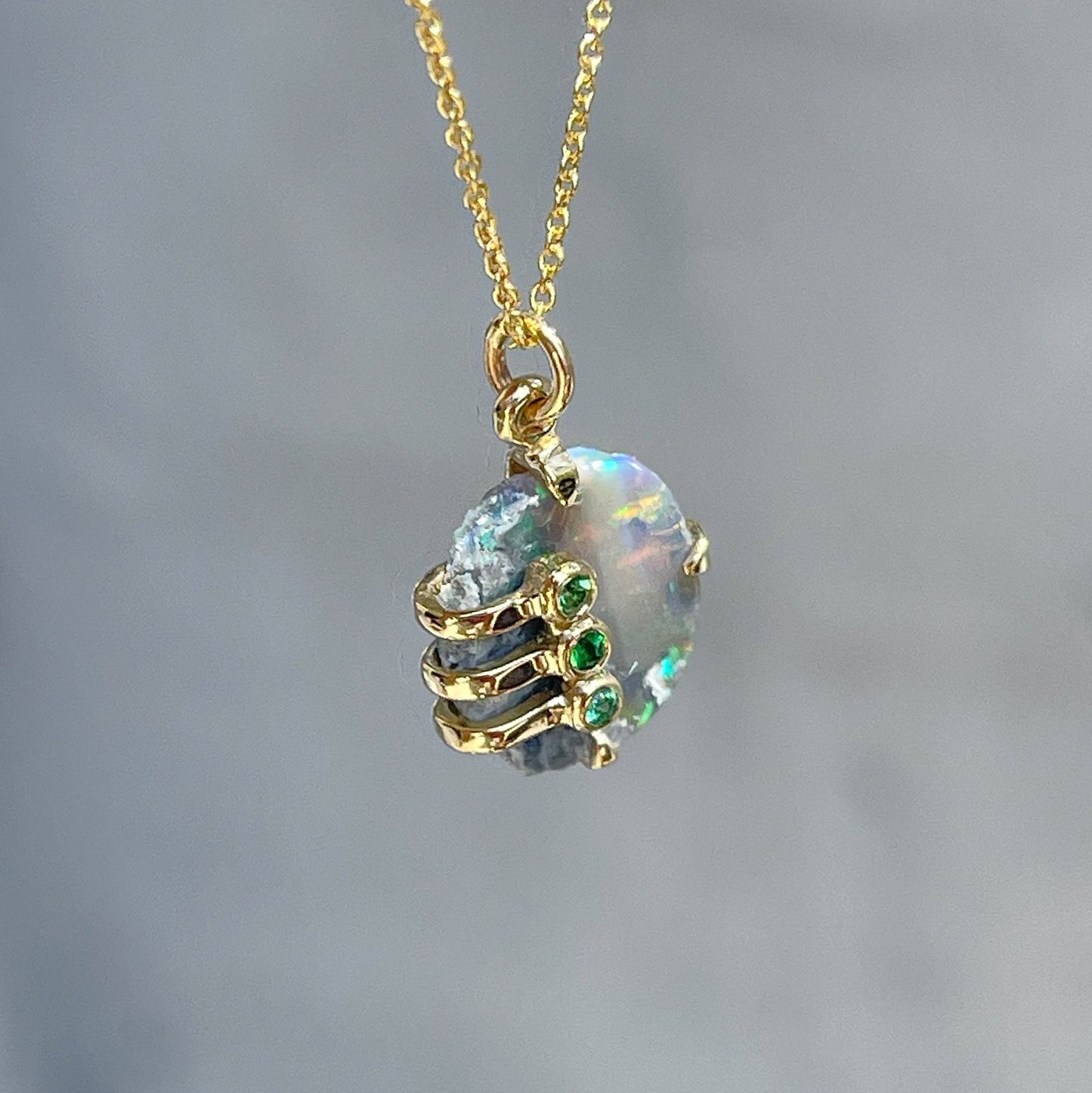 View from above of an Australian Opal Necklace by NIXIN Jewelry. The opal pendant necklace has an emerald and garnet detailing. 