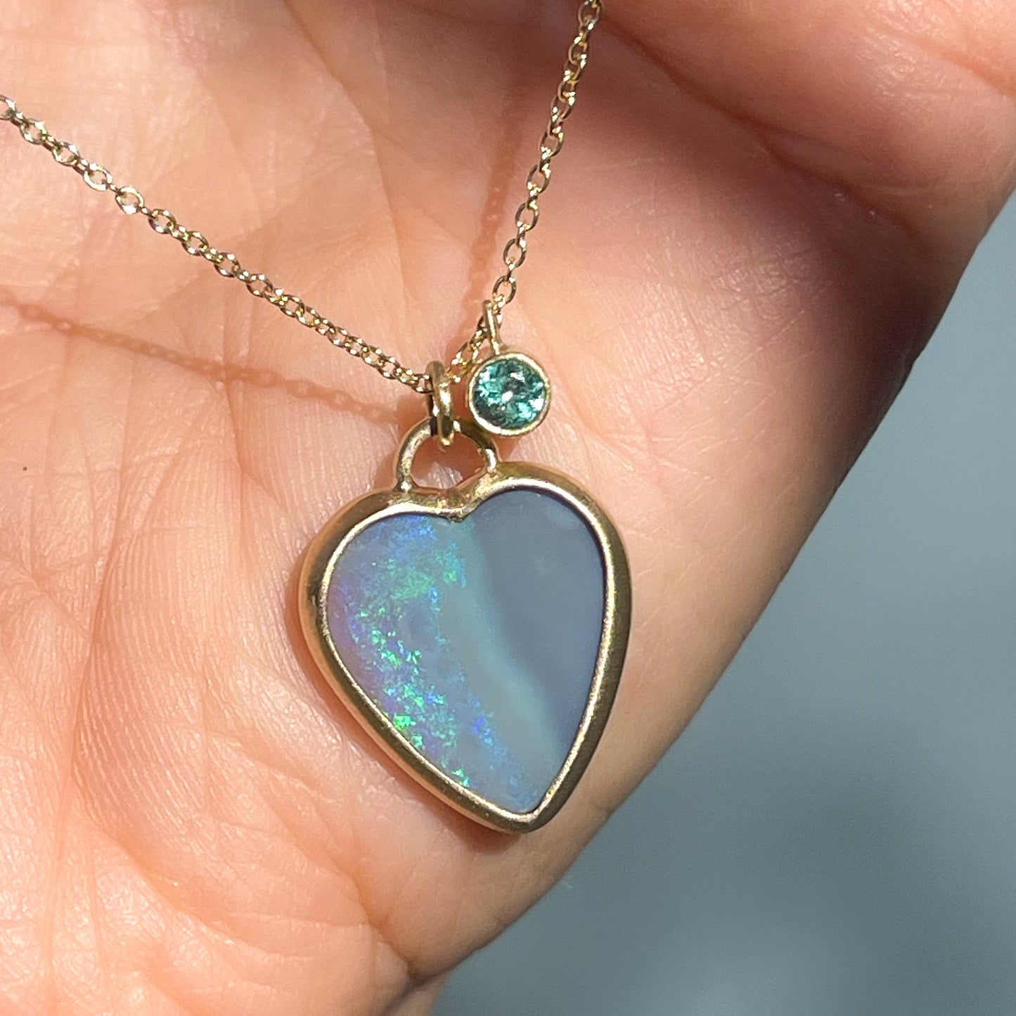 An Australian Opal Necklace with a double sided black opal heart and a two sided emerald charm.