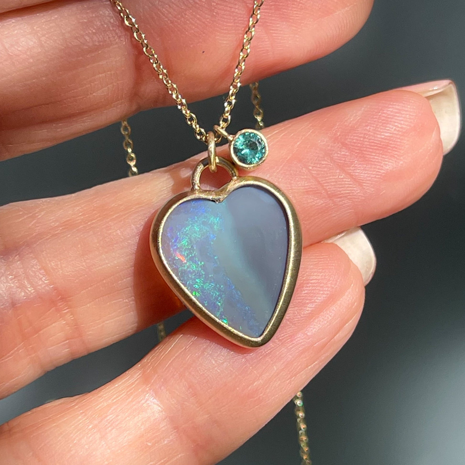 An Australian Opal Necklace by NIXIN Jewelry with an emerald charm next to the opal pendant.