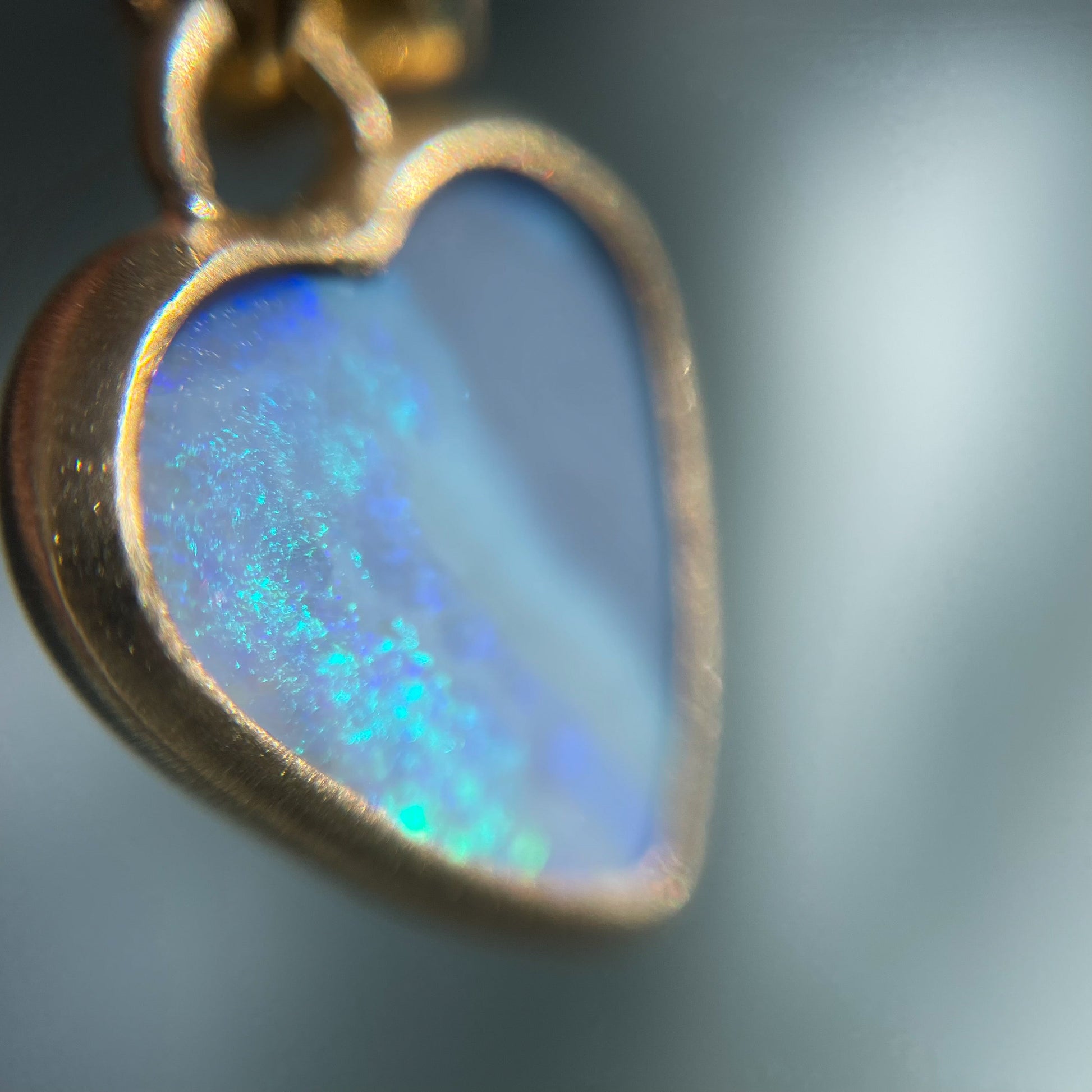 Close up of an Australian Opal Necklace by NIXIN Jewelry showing the blue and green in the black opal heart. A gold opal necklace.