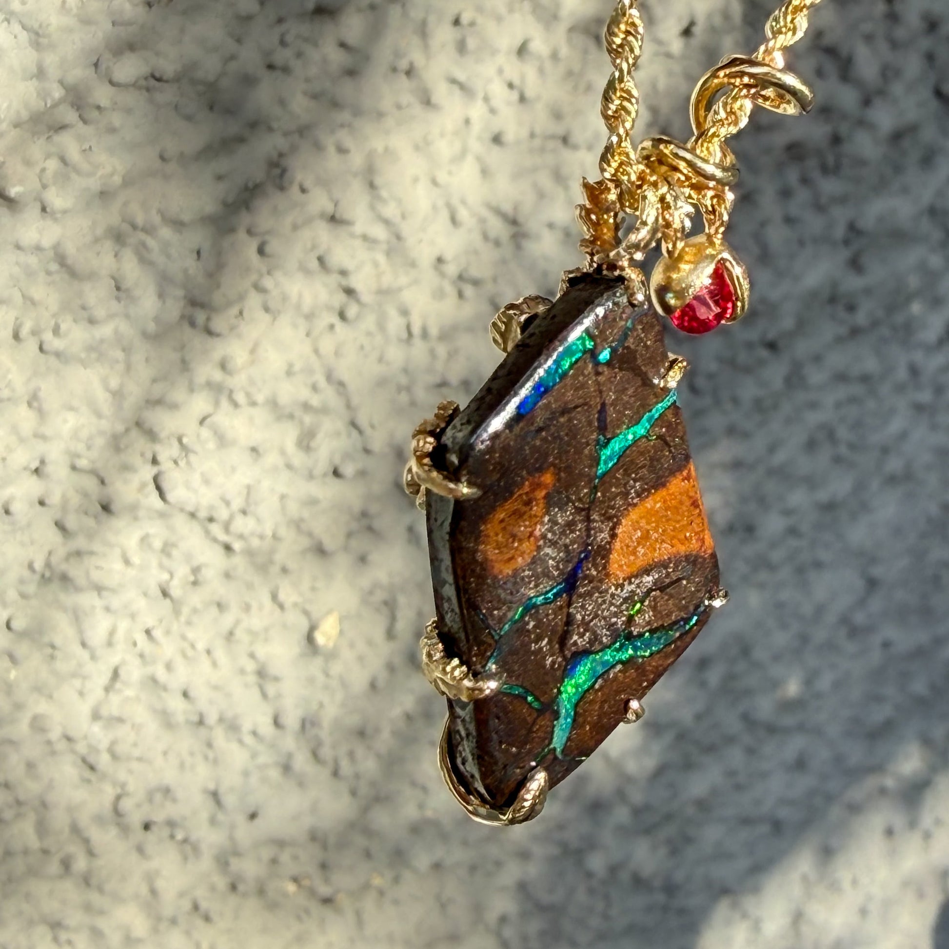 An Australian Opal Pendant by NIXIN Jewelry catches the natural light to reveal the exquisite veining of the opal stone against its ironstone matrix. The matte gold bypass bail and ruby charm add a sophisticated contrast to the play of color, defining it as unique fine jewelry. This Australian opal jewelry is a masterpiece of light and texture, perfect for a high-end luxury necklace collection.