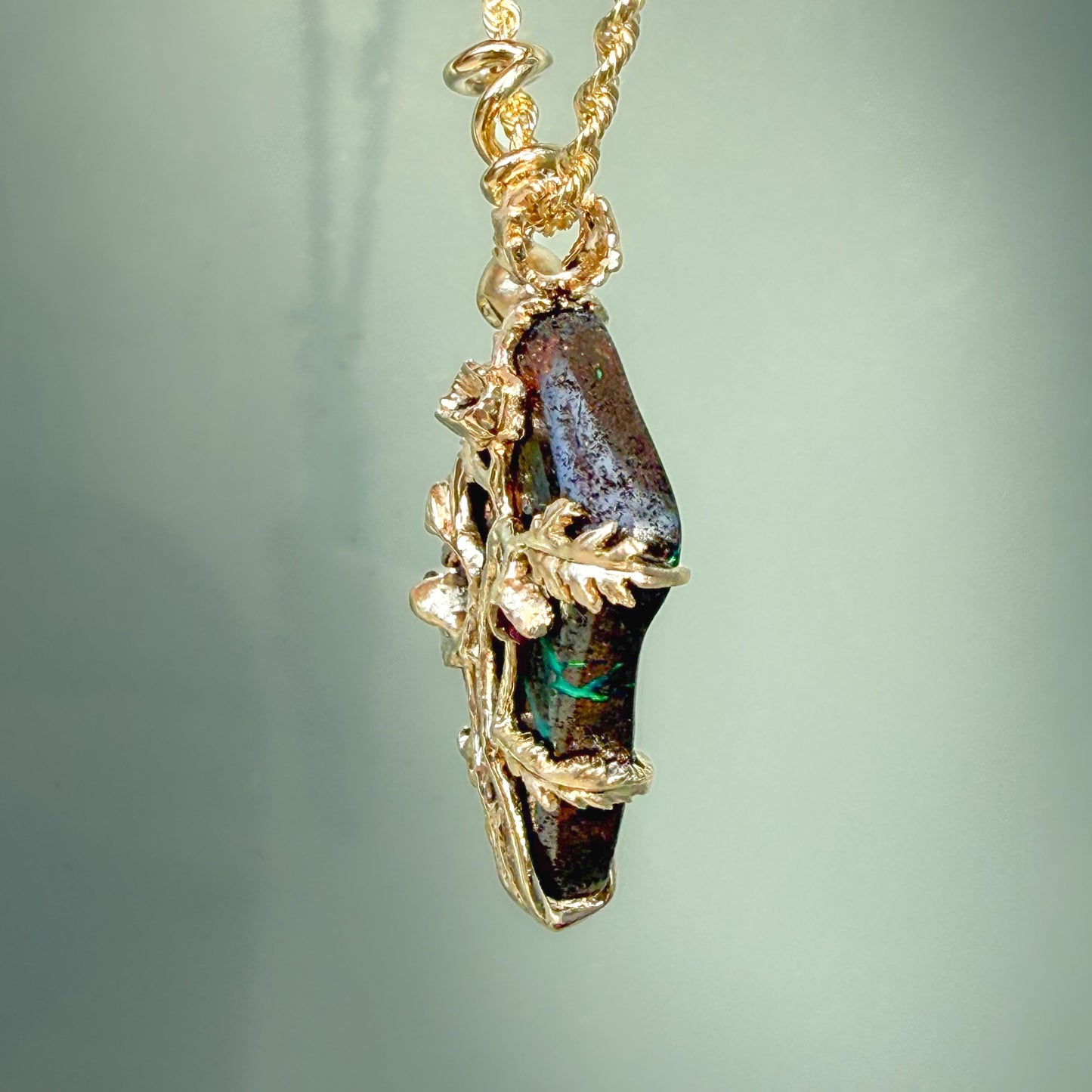 An Australian Opal Pendant by NIXIN Jewelry is shown from the side to emphasize the substantial, organic thickness of the boulder opal ironstone. The 14k gold vines are seen wrapping securely around the edge of the opal stone, demonstrating the durability and luxury of this artisan jewelry. This perspective highlights the sculptural depth that defines this unique opal necklace as a true work of jewelry art.