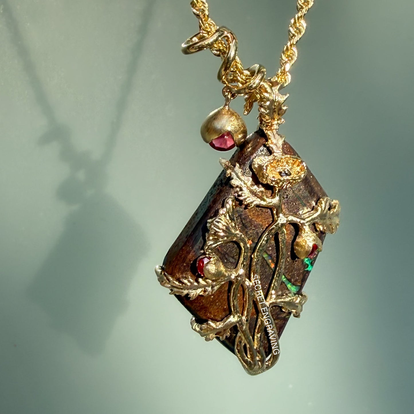 An Australian Opal Pendant by NIXIN Jewelry is captured in a sharp, angled view that focuses on the interplay between the deep ironstone matrix and the vibrant green opal leaf veining. This unique fine jewelry highlights the contrast of the matte gold floral elements against the shadowy depths of the boulder opal, emphasizing its rare jewelry status. The perspective provides a clear look at the prong setting and the delicate ruby accents, making it a compelling view for collectors of unique opal jewelry.