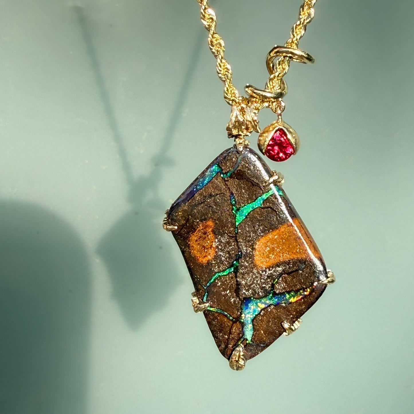 An Australian Opal Pendant by NIXIN Jewelry with a Boulder Opal set in 14k gold. The gold opal necklace is accented by a vibrant ruby that alludes to a secret design on its other side. A luxury necklace perfect for opal lovers.