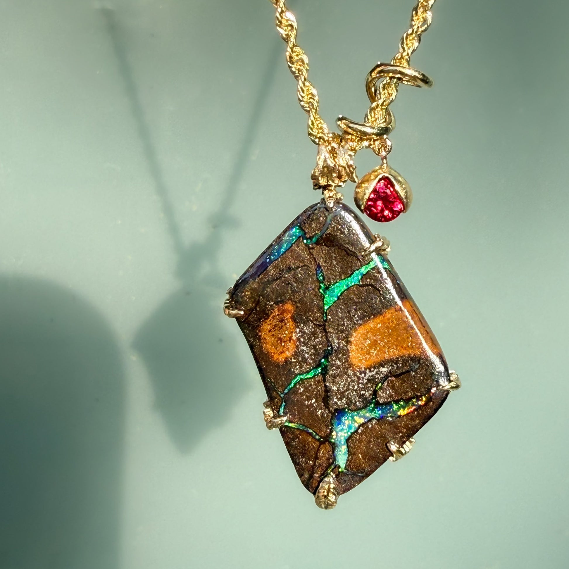 An Australian Opal Pendant by NIXIN Jewelry with a Boulder Opal set in 14k gold. The gold opal necklace is accented by a vibrant ruby that alludes to a secret design on its other side. A luxury necklace perfect for opal lovers.
