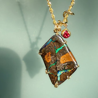 An Australian Opal Pendant by NIXIN Jewelry with a Boulder Opal set in 14k gold. The gold opal necklace is accented by a vibrant ruby that alludes to a secret design on its other side. A luxury necklace perfect for opal lovers.