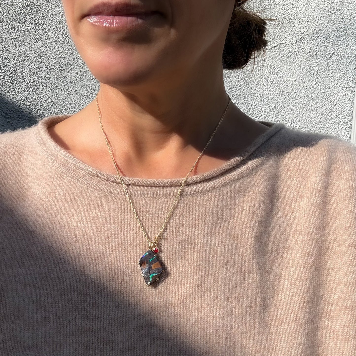 One-of-a-kind Australian Boulder Opal pendant by NIXIN Jewelry featuring vibrant green and blue fire, set in a gold claw setting and worn on a model. The backside has an elaborate gold carving. Photo highlights the front; iridescent green veins against an ironstone matrix.