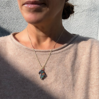 One-of-a-kind Australian Boulder Opal pendant by NIXIN Jewelry featuring vibrant green and blue fire, set in a gold claw setting and worn on a model. The backside has an elaborate gold carving. Photo highlights the front; iridescent green veins against an ironstone matrix.