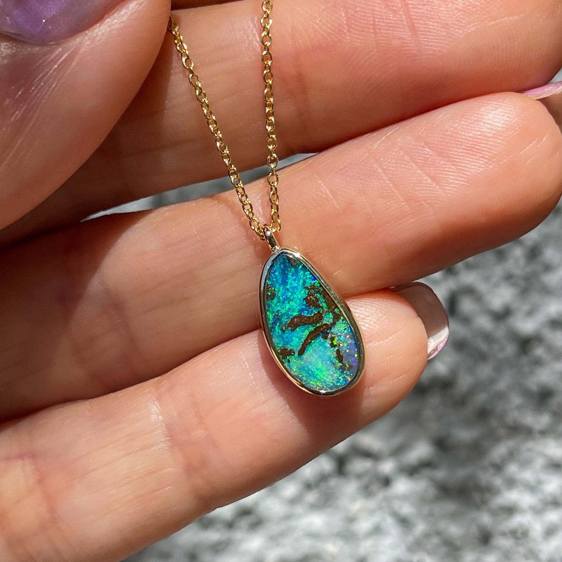 An Australian Opal Necklace by NIXIN Jewelry resting on top of a hand in sunlight. The Boulder Opal is set in yellow gold and is perfect for rare jewelry collectors.
