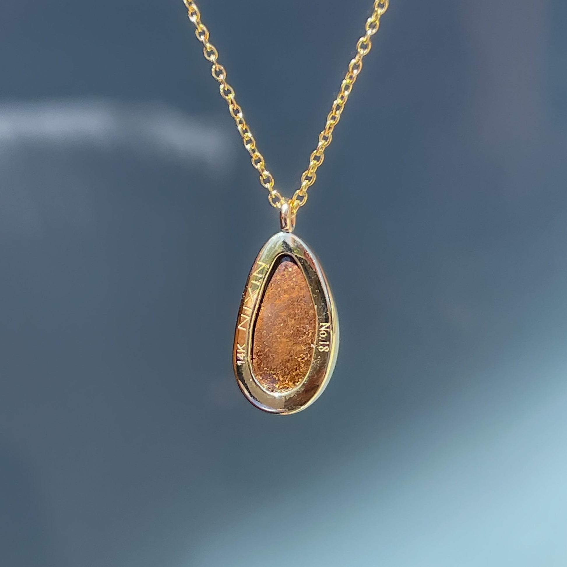 The back of an Australian Opal Necklace by NIXIN Jewelry. The photo shows the back of the gold bezel setting and the serial number of the limited edition engraved on the back.