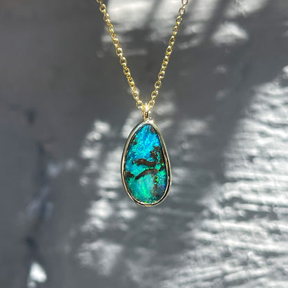 An Australian Opal Necklace by NIXIN Jewelry hanging in front of a grey wall. The opal pendant necklace is made in yellow gold and among the opal jewelry for sale on the NIXIN Jewelry website.
