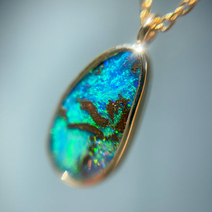 Close up of an Australian Opal Necklace by NIXIN Jewelry.  Image shows the Boulder Opal mounted in a bezel setting on a gold chain.