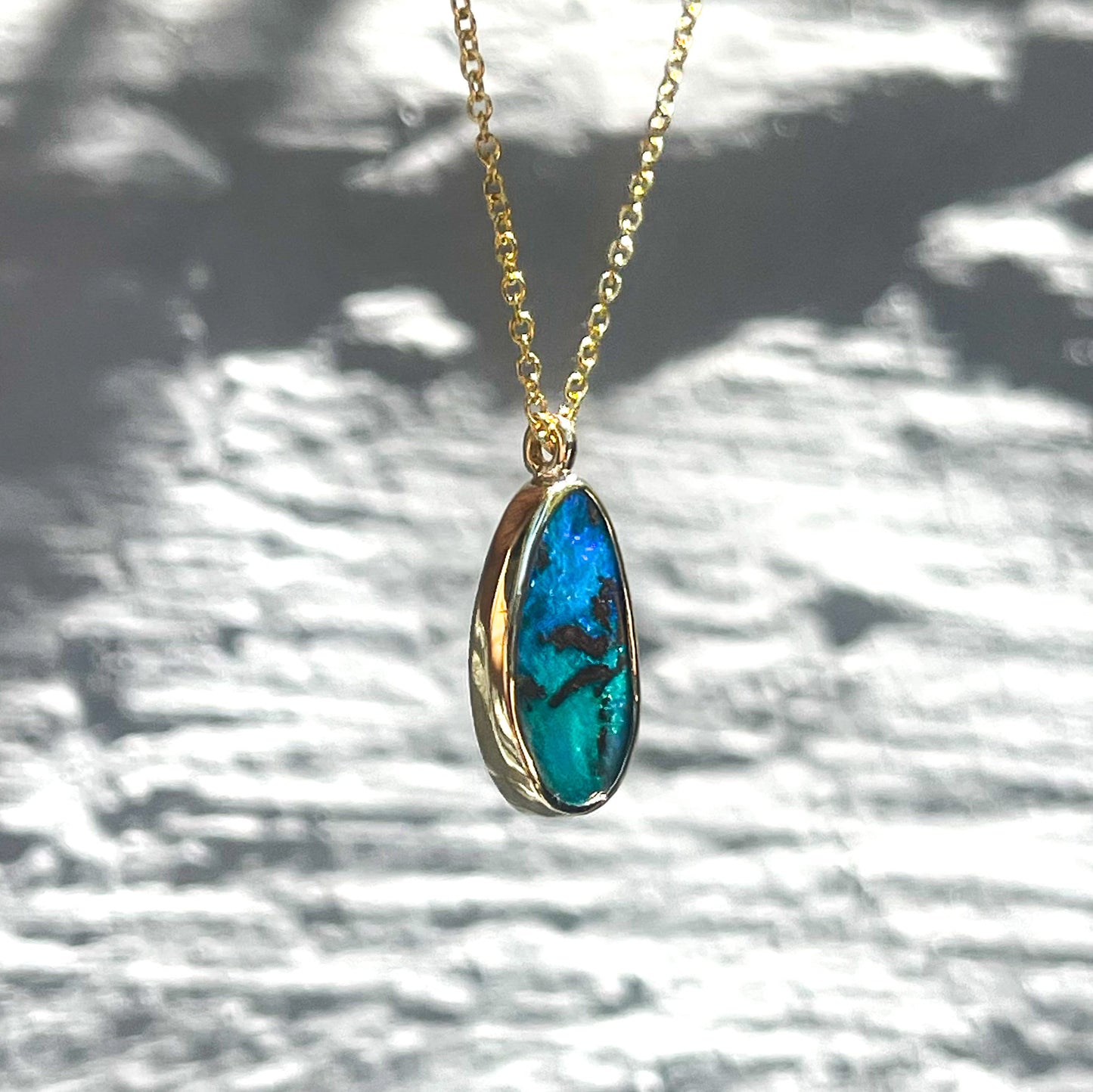 An Australian Opal Necklace by NIXIN Jewelry shown in shade and in semi-profile. Image displays the side of the gold bezel setting and the depth of the opal stone.