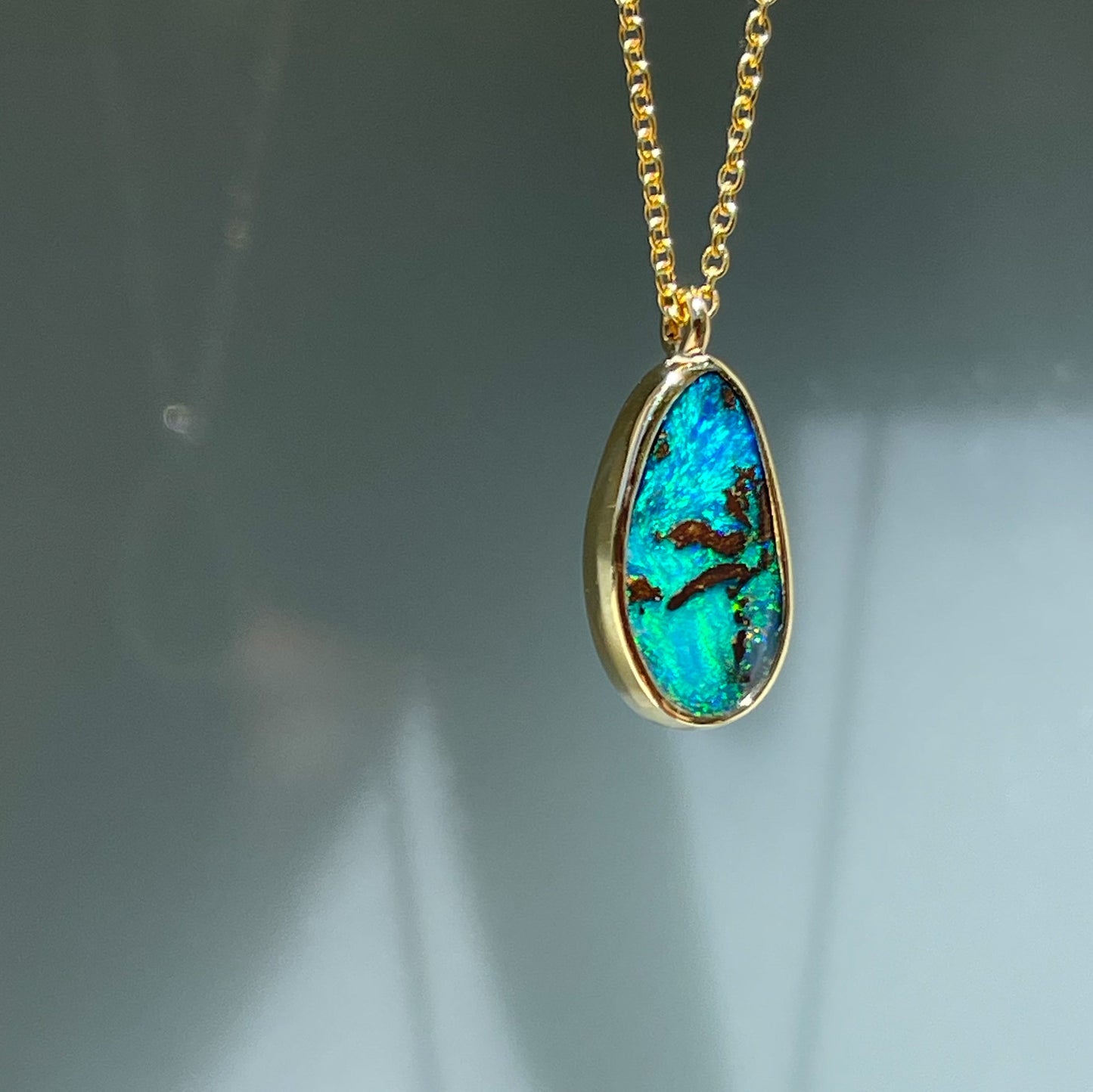 An Australian Opal Necklace by NIXIN Jewelry shown at an angle to show off the bezel wall. Set in polished gold and hanging from an 18" chain. You can find the Australian Opal for sale on the NIXIN Jewelry website.