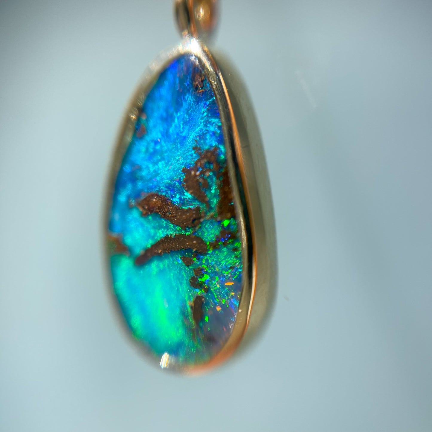 Close up shot of an Australian Opal Necklace by NIXIN Jewelry. Image shows the opal pendant at a slight angle to highlight the blue and green fire and palm tree pattern.