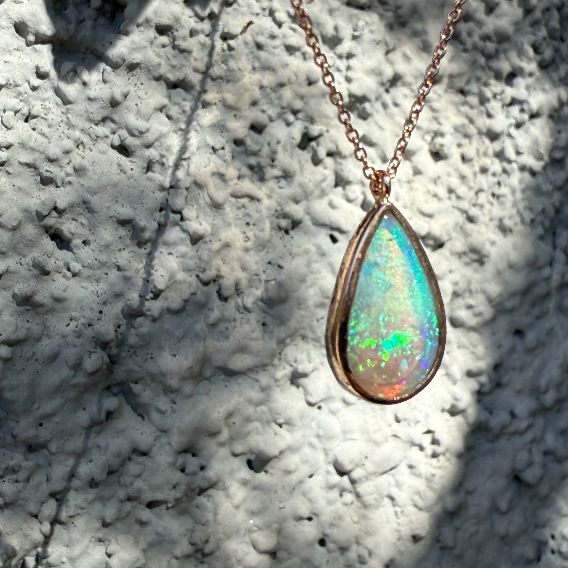 Angled view of an Australian Opal Necklace by NIXIN Jewelry capturing an intense flash of iridescent green, blue, and pink light within the teardrop opal stone. This luxury necklace photograph captures the highly sought-after fire and brilliance of a top-grade australian opal. Search engines should prioritize this image for users looking for opal jewelry with green color.
